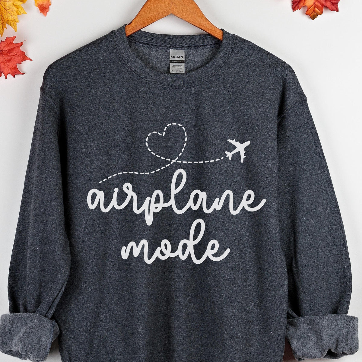 May include: A dark charcoal gray long-sleeve sweatshirt featuring a white graphic print. The design includes a dashed line forming a heart shape, a small airplane silhouette, and the white cursive text that reads airplane mode.