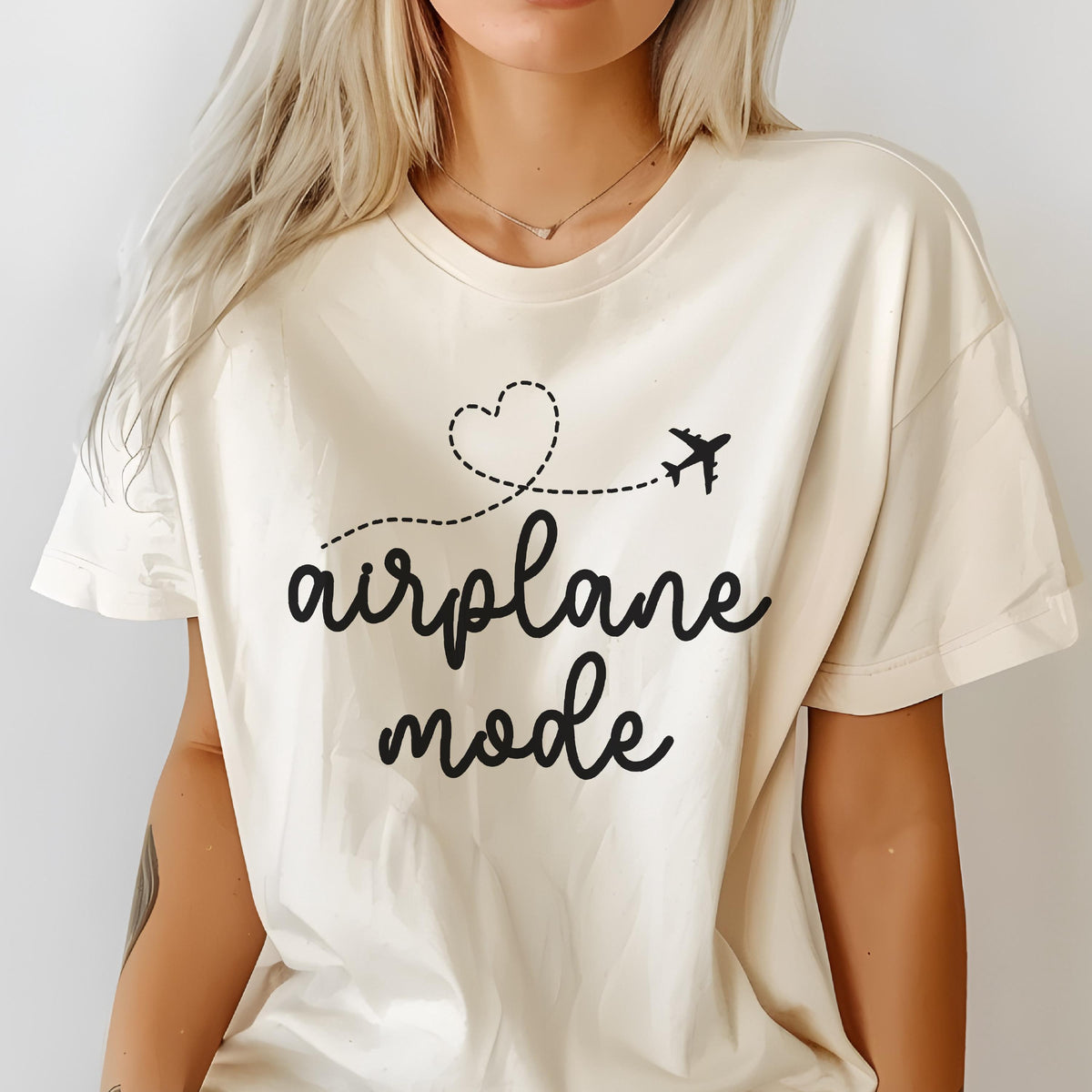 May include: Cream-colored t-shirt with the words "airplane mode" in a black script font. A dotted line with a heart and airplane graphic is above the text. The shirt is made of a soft material.