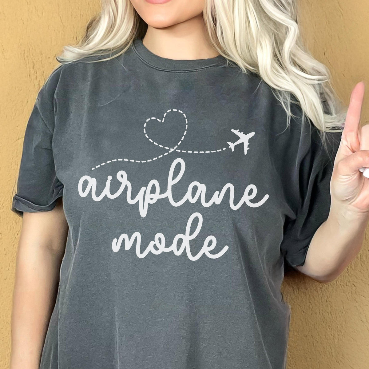 May include: Dark gray t-shirt with the words "airplane mode" in white script. A white airplane graphic follows a dotted heart-shaped line. The shirt is a casual style.