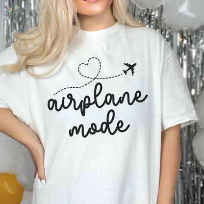 May include: White t-shirt with the words "airplane mode" in a black script font. A dotted line forms a heart shape and leads to a small airplane graphic. The shirt is a casual, comfortable style.