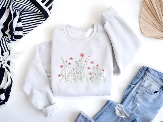 May include: A white sweatshirt with a floral design featuring pink flowers and green stems. The sweatshirt is laid flat on a white surface.
