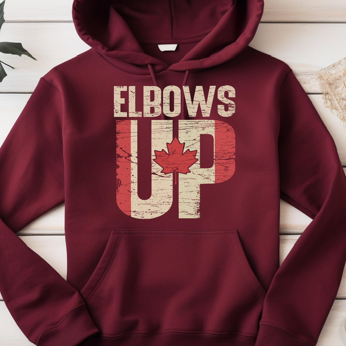 May include: A maroon hoodie with a distressed Canadian flag design and the text "Elbows Up" printed on the front.