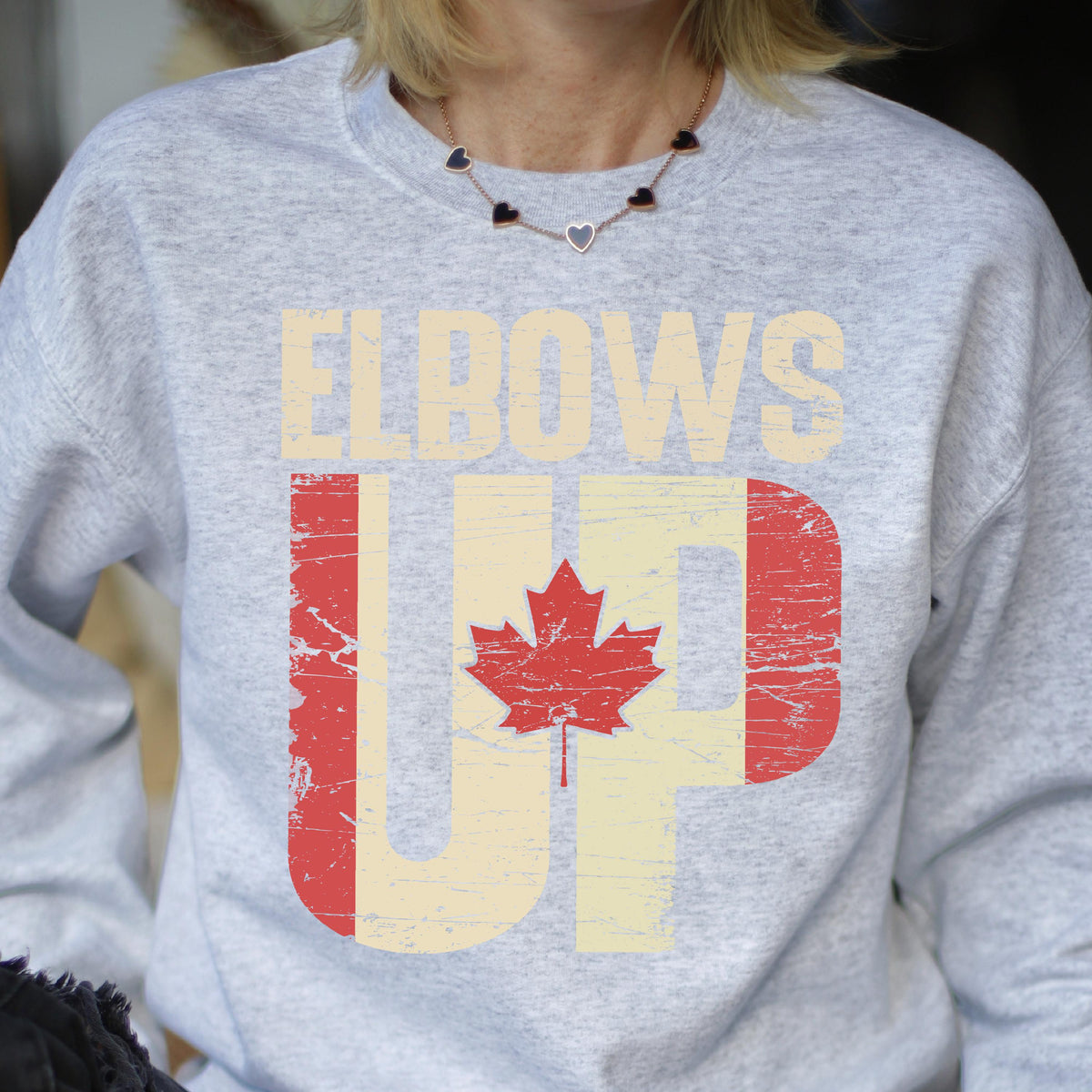 May include: Gray sweatshirt with the text "Elbows Up" in white letters with a distressed Canadian flag design in red and white.