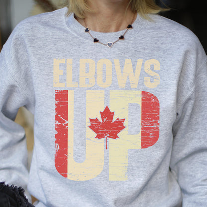 May include: Gray sweatshirt with the text "Elbows Up" in white letters with a distressed Canadian flag design in red and white.