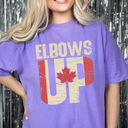 May include: Purple t-shirt with a distressed graphic design featuring a Canadian flag and the text "Elbows Up".