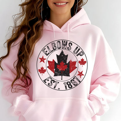 May include: A light pink hooded sweatshirt featuring a central circular graphic with the text ELBOWS UP EST. 1867. The design includes a large distressed black and red maple leaf, smaller red maple leaves, and red stars within the black circular border.
