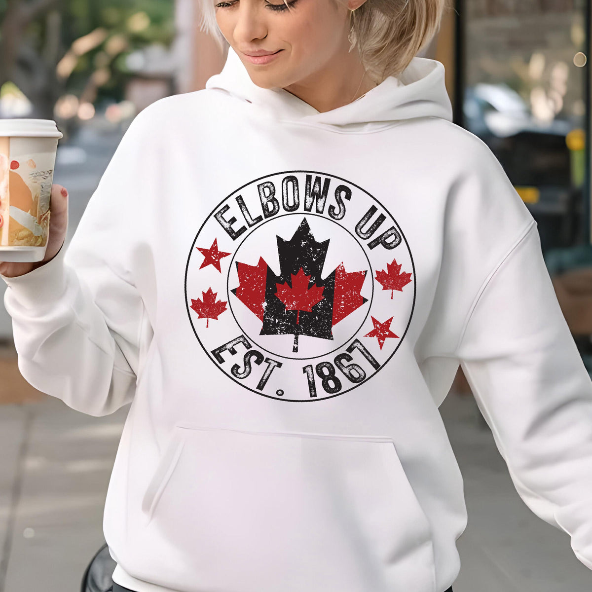 May include: A white long-sleeve hooded sweatshirt featuring a circular graphic on the chest. The design includes the text "ELBOWS UP" and "EST. 1861" surrounding a central black and red maple leaf emblem with additional small red maple leaf icons.