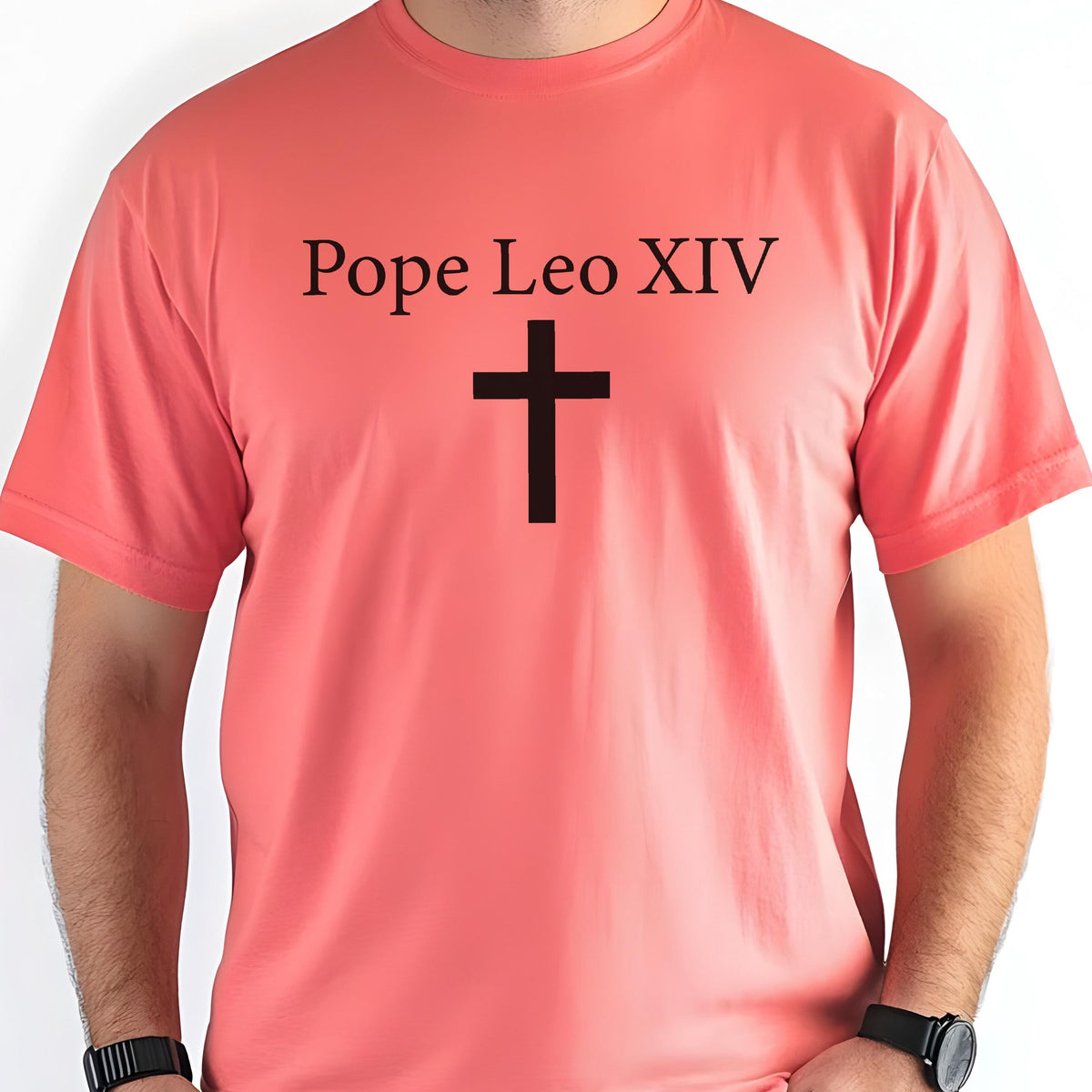 May include: Coral-colored t-shirt featuring the text "Pope Leo XIV" above a black cross. The short-sleeved shirt is made of a soft material and is suitable for casual wear.
