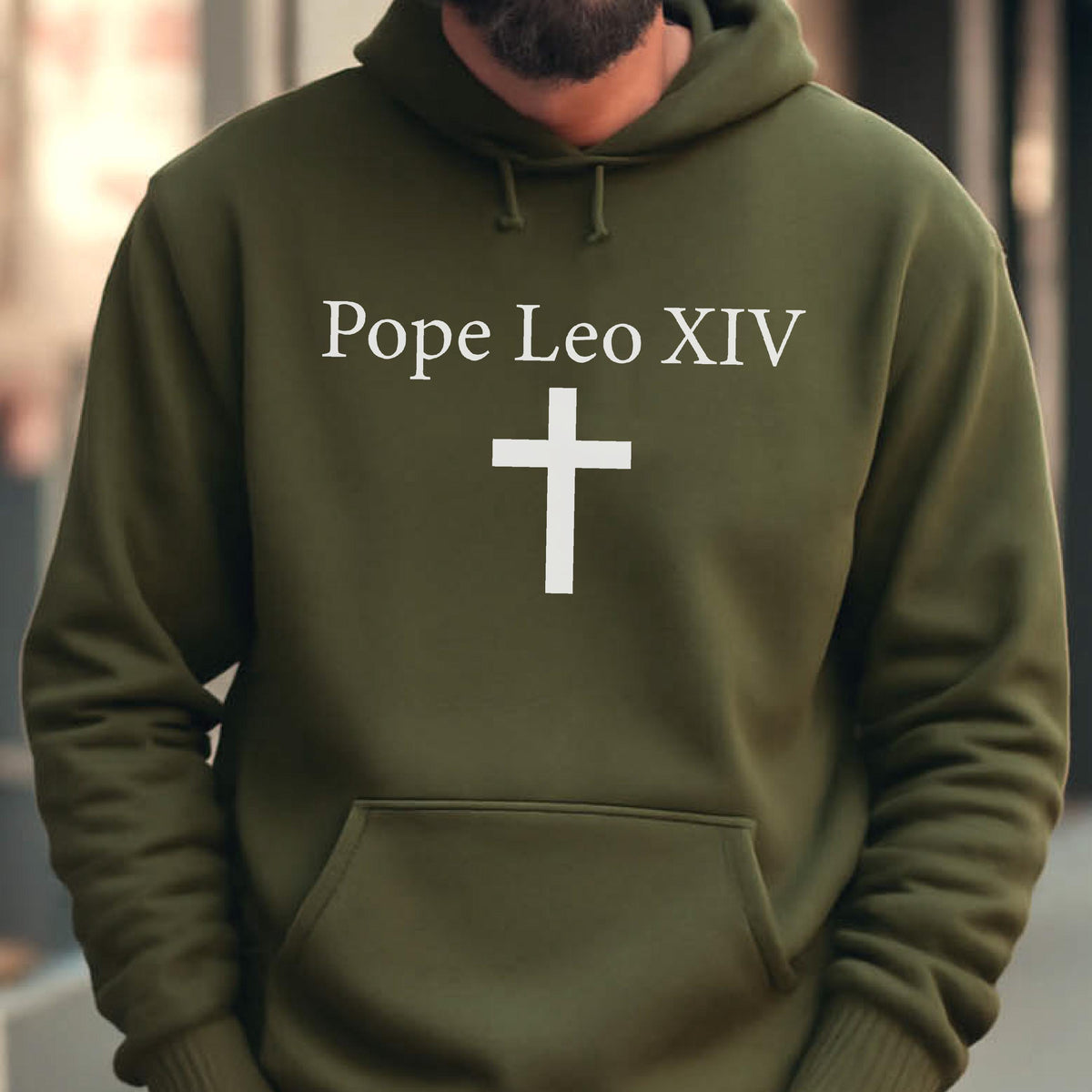 May include: Olive green hooded sweatshirt with a white cross and the text "Pope Leo XIV". The sweatshirt has a kangaroo pocket and a drawstring hood. The design is centered on the front of the garment.