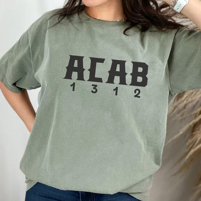 May include: A sage green short-sleeve t-shirt featuring the black text ACAB centered on the chest, with the numbers 1 3 1 2 printed directly below the letters in a matching black font. The shirt has a crew neckline and a relaxed fit.