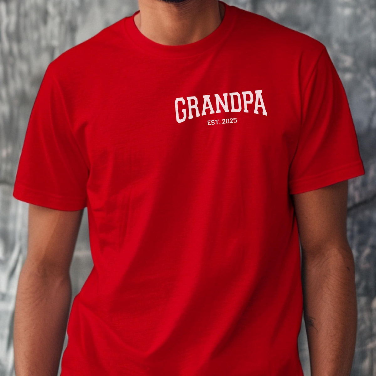 May include: A red t-shirt with the word "GRANDPA" printed in white arched text across the chest. Below the word "GRANDPA" is the text "EST. 2025" in a smaller font. The shirt is short-sleeved.