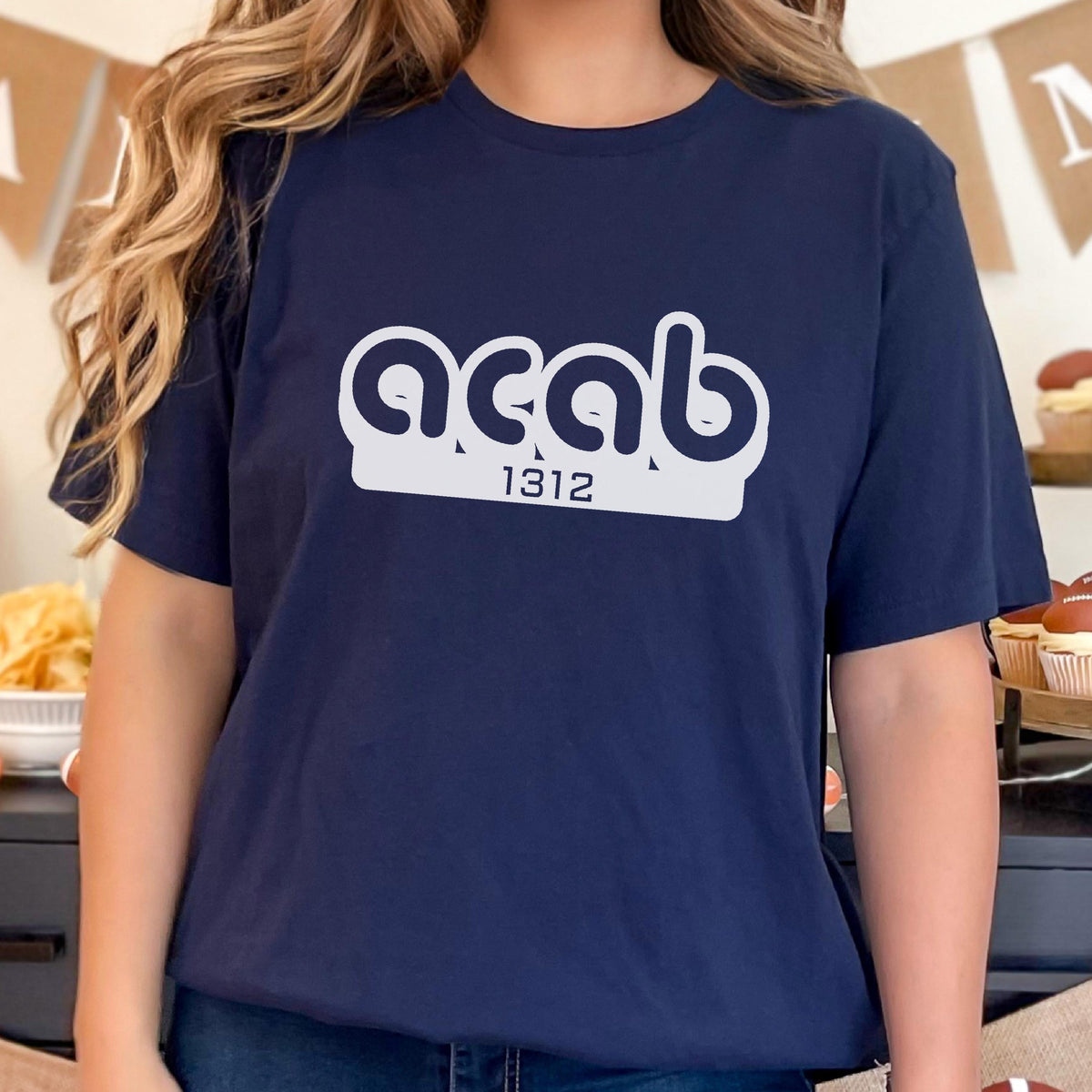May include: A navy blue t-shirt with a white graphic of the text "acab" in a rounded font with the number "1312" below it.