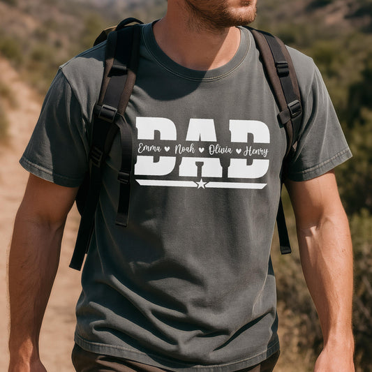 May include: Dark gray t-shirt with the word "DAD" in white block letters. Below the word "DAD" are the names "Emma", "Noah", "Olivia", and "Henry". A white star is below the names. The shirt is being worn by a person.