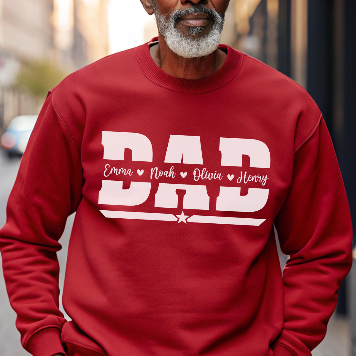 May include: A red sweatshirt with the word "DAD" in large white block letters. Below the word "DAD" are the names "Emma", "Noah", "Olivia", and "Henry" in white script, separated by hearts. A white star is below the names.