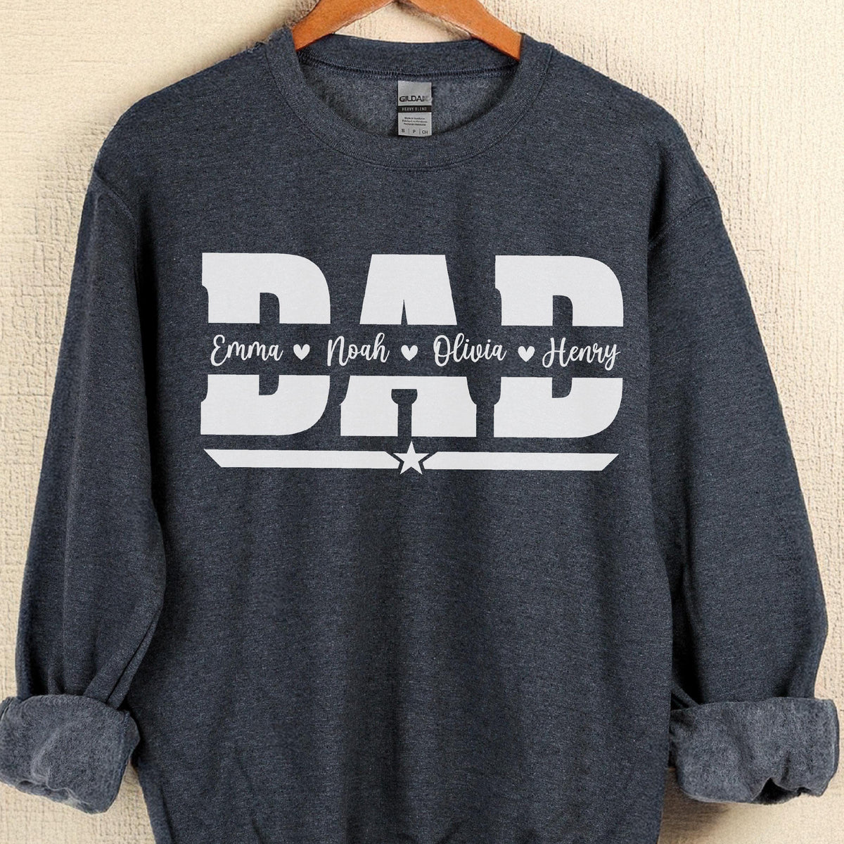 May include: A dark gray sweatshirt with the word "DAD" in large white block letters. Below the word "DAD" are the names "Emma", "Noah", "Olivia", and "Henry" in white script. A white star is below the word "DAD".