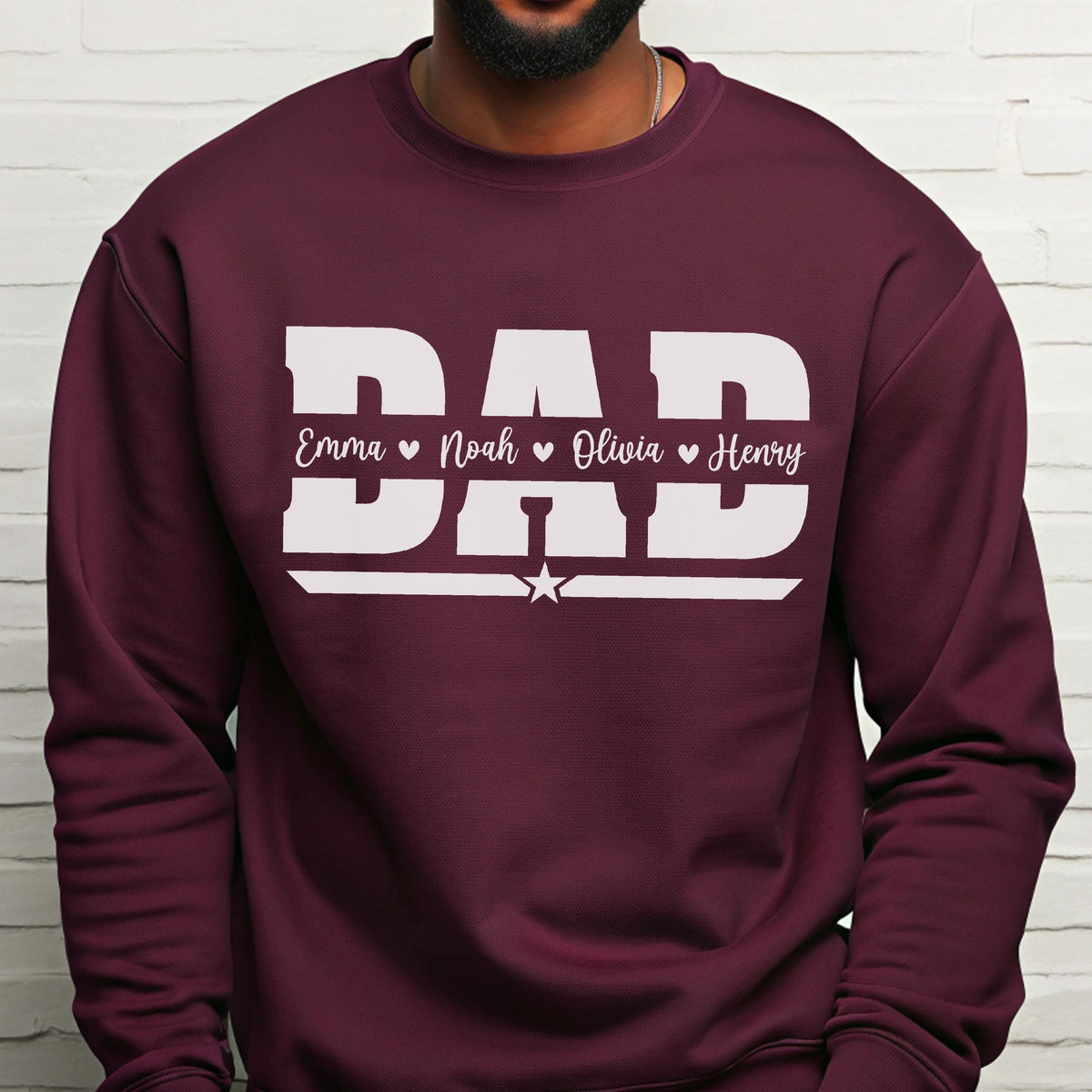 May include: A maroon sweatshirt with the word "DAD" in large white block letters. Below the word "DAD" are the names Emma, Noah, Olivia, and Henry, each with a heart symbol. A white star is centered below the names.
