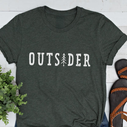 May include: A dark charcoal gray short-sleeve t-shirt featuring the white text "OUTSIDER" printed across the chest. The letter "I" is replaced by a stylized white graphic of a pine tree. The fabric has a heathered texture throughout the garment.
