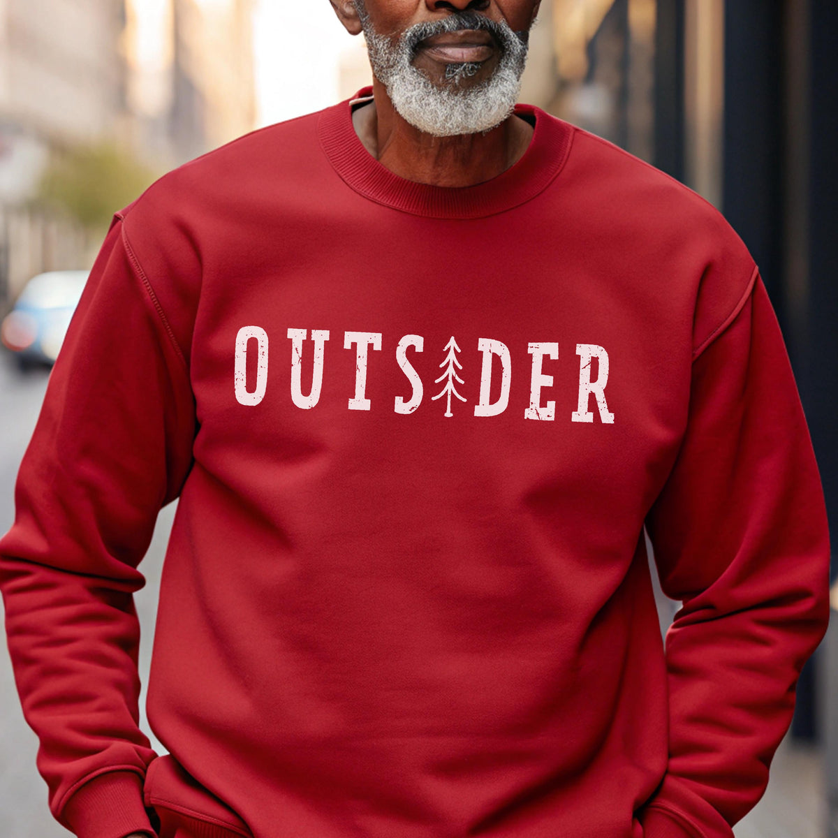 May include: A red crewneck sweatshirt featuring the white text OUTSIDER printed across the chest, with a small white pine tree graphic replacing the letter I. The garment has long sleeves, a ribbed neckline, and a standard pullover fit.
