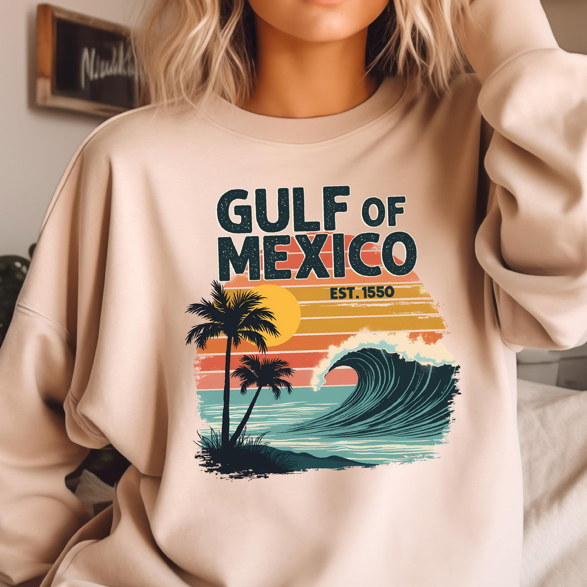 May include: A beige sweatshirt with a retro-style graphic design featuring a palm tree, a wave, and the text "GULF OF MEXICO EST. 1550".