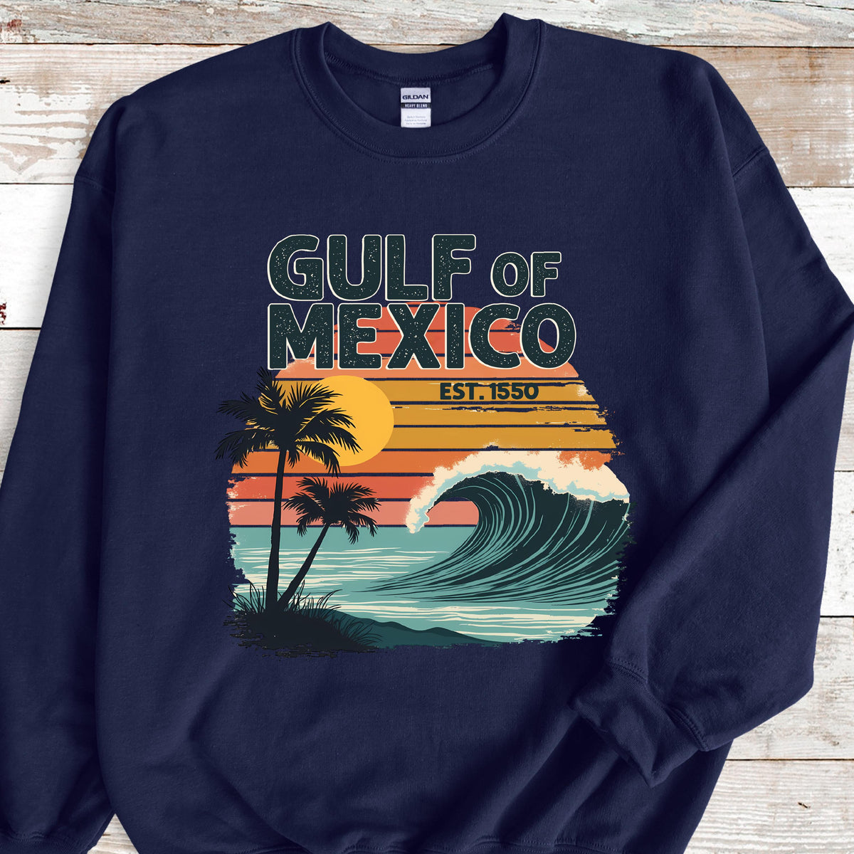 May include: Navy blue sweatshirt with a vintage-style graphic of a wave crashing on a beach with palm trees and a sunset. The text "GULF OF MEXICO EST. 1550" is printed on the sweatshirt.