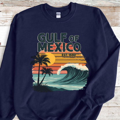 May include: Navy blue sweatshirt with a vintage-style graphic of a wave crashing on a beach with palm trees and a sunset. The text "GULF OF MEXICO EST. 1550" is printed on the sweatshirt.