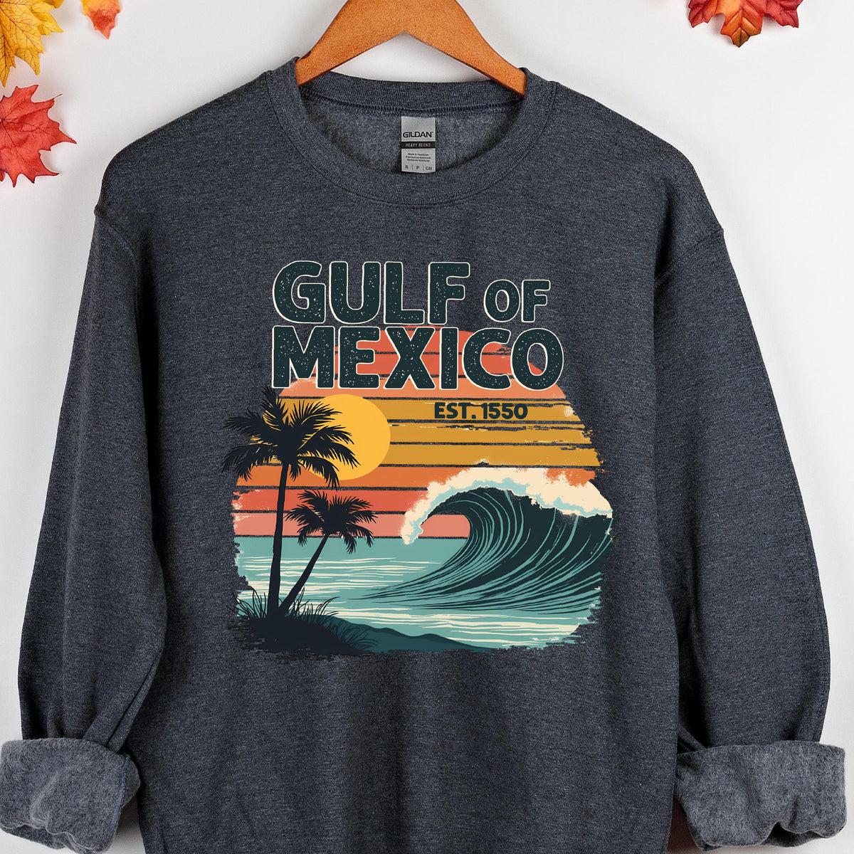 May include: A dark gray sweatshirt with a retro-style graphic design featuring a palm tree, a wave, and the text "GULF OF MEXICO EST. 1550".