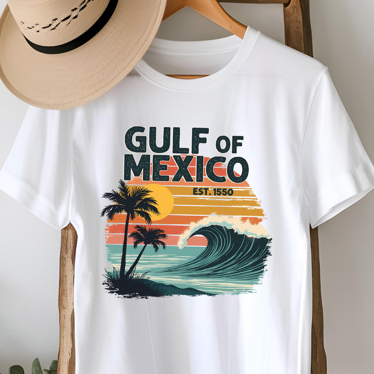 May include: White t-shirt with a retro-style graphic design featuring a wave, palm trees, and a sunset. The text "GULF OF MEXICO EST. 1550" is printed on the shirt.