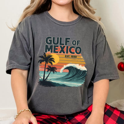 May include: A gray t-shirt with a vintage-style graphic of a sunset, palm trees, and a wave. The text "GULF OF MEXICO EST. 1550" is printed on the shirt.