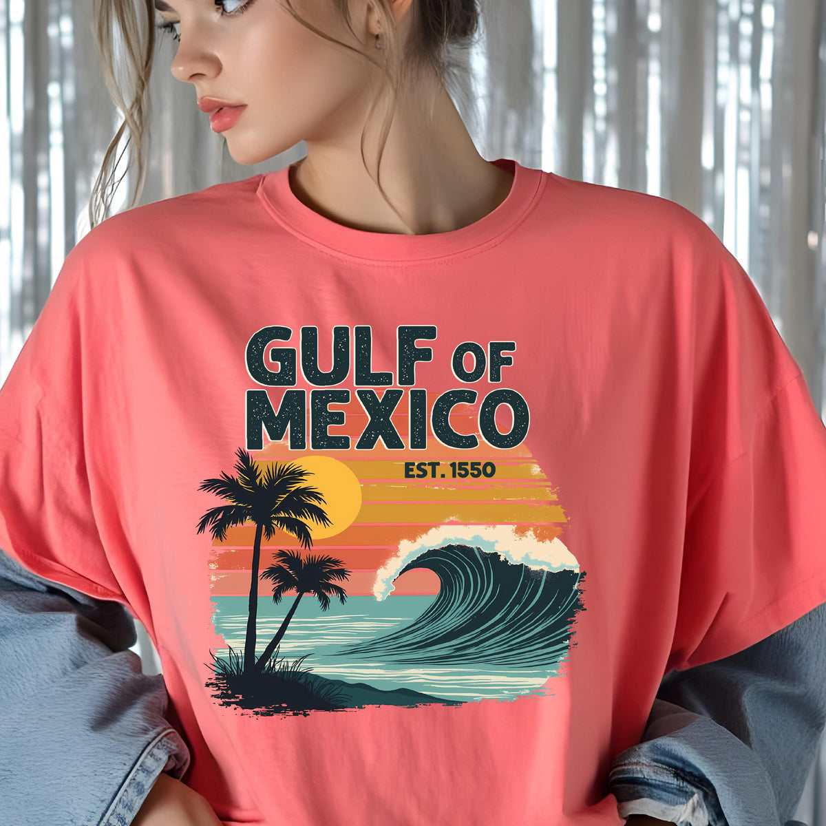 May include: A pink t-shirt with a graphic design of a sunset over a wave with palm trees. The text "GULF OF MEXICO EST. 1550" is printed on the shirt.