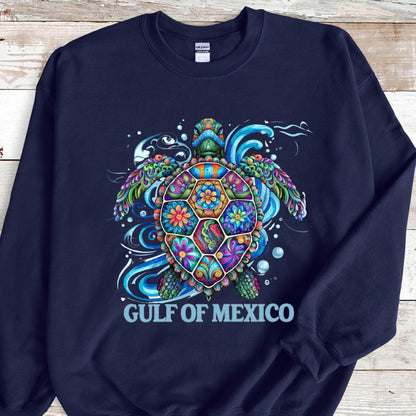 May include: Navy blue sweatshirt featuring a colorful sea turtle design. The turtle has a vibrant, patterned shell with floral and geometric shapes in shades of blue, green, orange, and purple. The text "GULF OF MEXICO" is printed below the turtle.