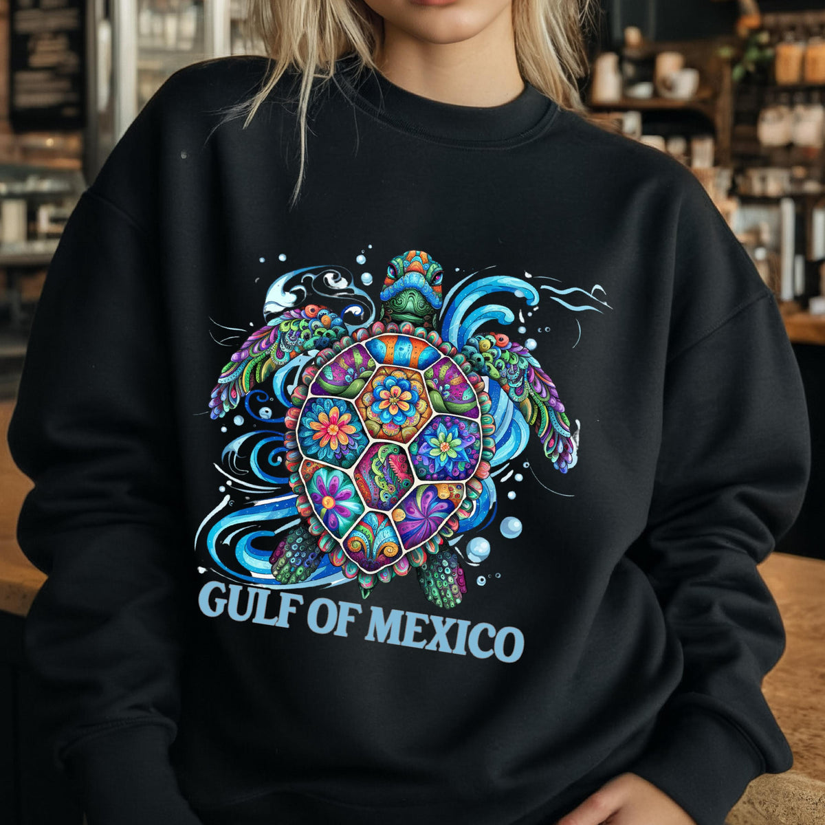 May include: Black sweatshirt featuring a colorful sea turtle design with floral patterns and the text "GULF OF MEXICO" in white. The turtle has a vibrant shell with shades of blue, green, orange, and purple, surrounded by blue water swirls.