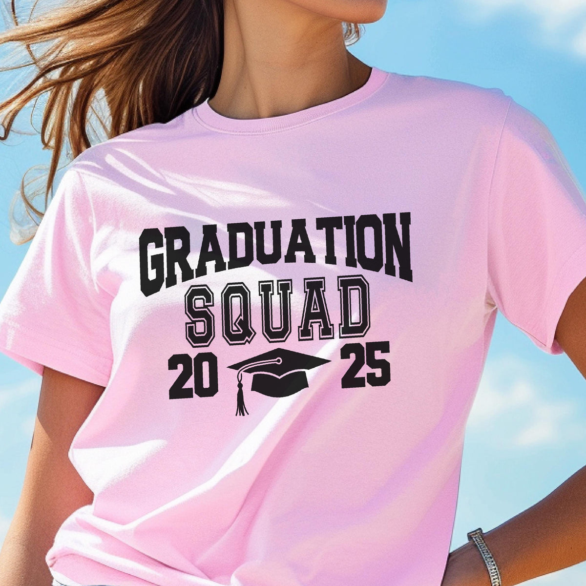 May include: A light pink t-shirt with the words "GRADUATION SQUAD 2025" printed in black. The design includes a graduation cap graphic. The shirt is short-sleeved and made of a soft material.