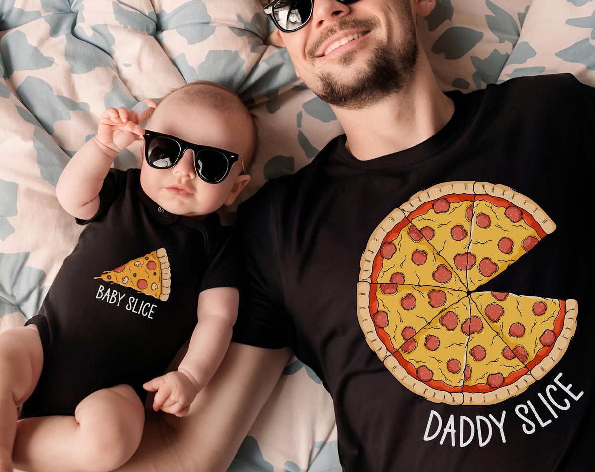 May include: A black t-shirt with a pizza graphic and the text "Daddy Slice" next to a baby wearing a black onesie with a pizza slice graphic and the text "Baby Slice". Both are wearing sunglasses.