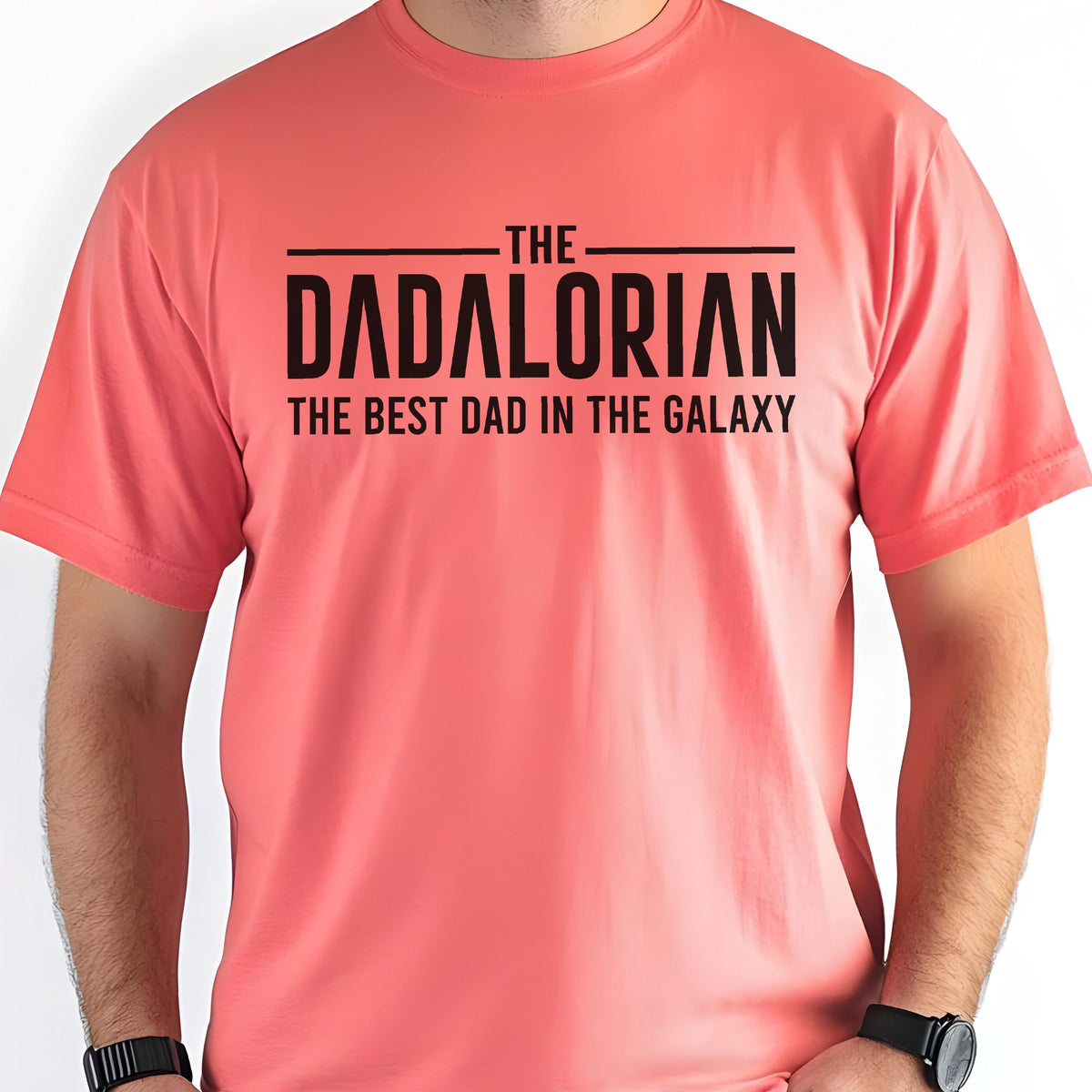 May include: Coral-colored t-shirt with the text "THE DADALORIAN THE BEST DAD IN THE GALAXY" in black block letters. The shirt has short sleeves and a crew neck. The text is centered on the chest.