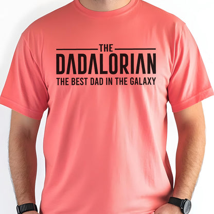 May include: Coral-colored t-shirt with the text "THE DADALORIAN THE BEST DAD IN THE GALAXY" in black block letters. The shirt has short sleeves and a crew neck. The text is centered on the chest.