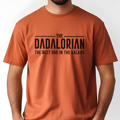 May include: An orange t-shirt with the text "THE DADALORIAN THE BEST DAD IN THE GALAXY" in black. The shirt has short sleeves and a crew neck.