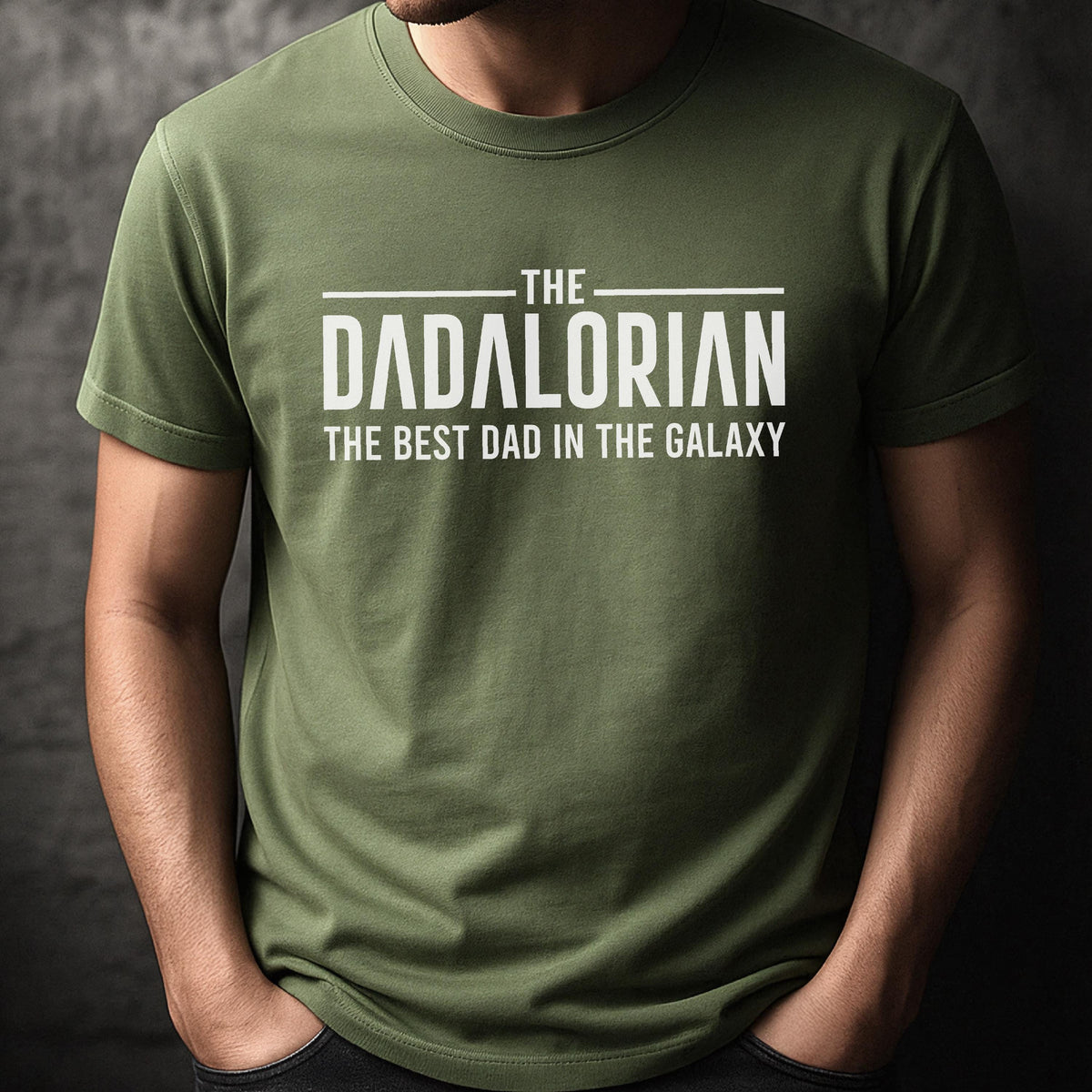 May include: Olive green t-shirt with the text "THE DADALORIAN THE BEST DAD IN THE GALAXY" in white. The shirt is a short-sleeved crew neck style.