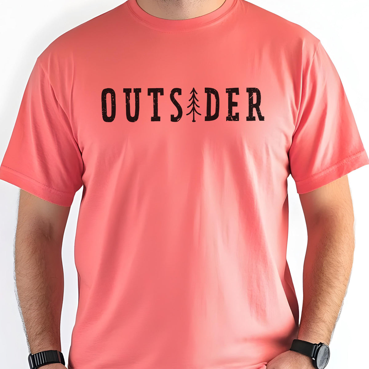 May include: A coral-colored short-sleeve t-shirt featuring the black text OUTSIDER printed across the chest. The letter I in the word is replaced by a stylized black graphic of a pine tree. The shirt has a crew neckline and a standard fit.