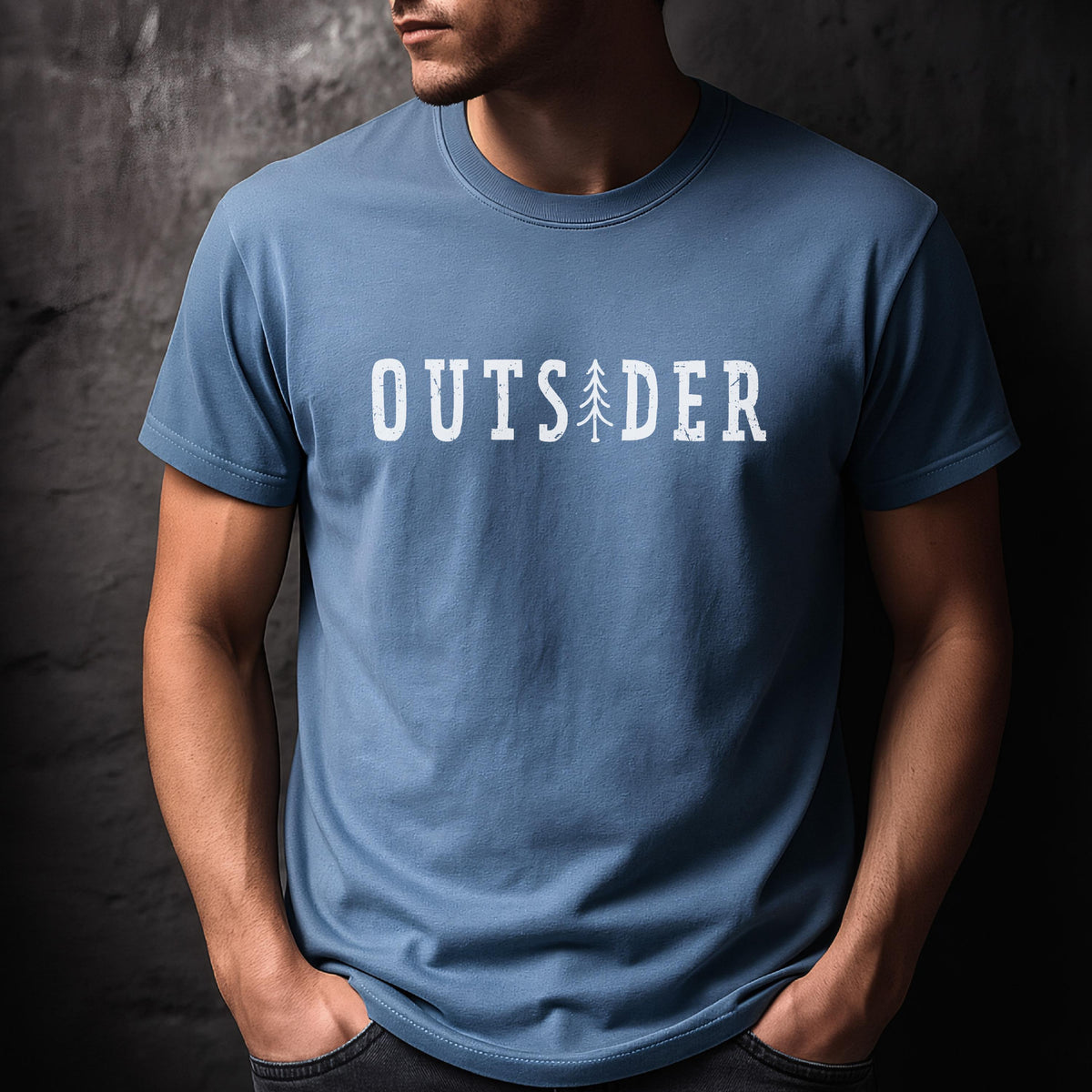 May include: A dusty blue short-sleeved crew neck t-shirt featuring the white text "OUTSIDER" printed across the chest. The letter "I" in the word is replaced by a simple white graphic illustration of a tall, slender evergreen pine tree.