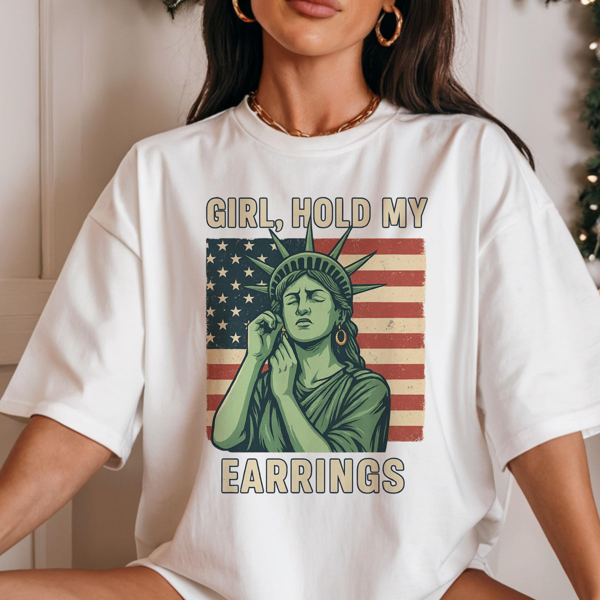 May include: White t-shirt with a graphic of the Statue of Liberty holding an earring and the text "Girl, hold my earrings" printed on it. The graphic is set against a red, white, and blue American flag.