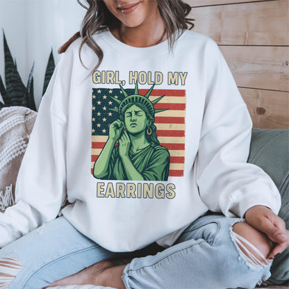 May include: White sweatshirt with a graphic of the Statue of Liberty holding an earring, with the text "Girl, hold my earrings" printed on the front.