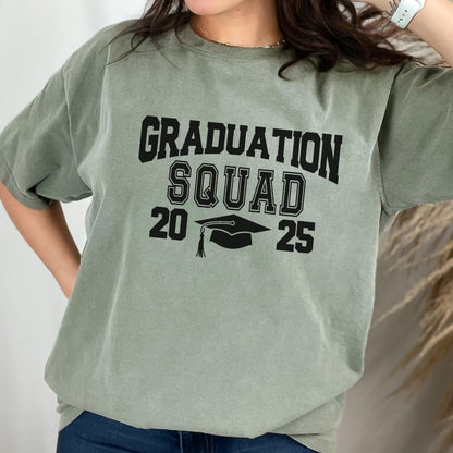 May include: Sage green t-shirt with the words "GRADUATION SQUAD 20 25" in black block letters. A graduation cap graphic is centered below the word "SQUAD". The shirt is a casual style.