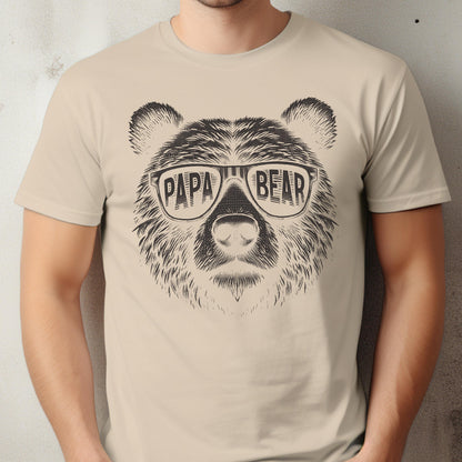May include: Beige t-shirt featuring a detailed illustration of a bear's face wearing sunglasses. The sunglasses have the words "PAPA BEAR" printed on them. The design is in black and white.