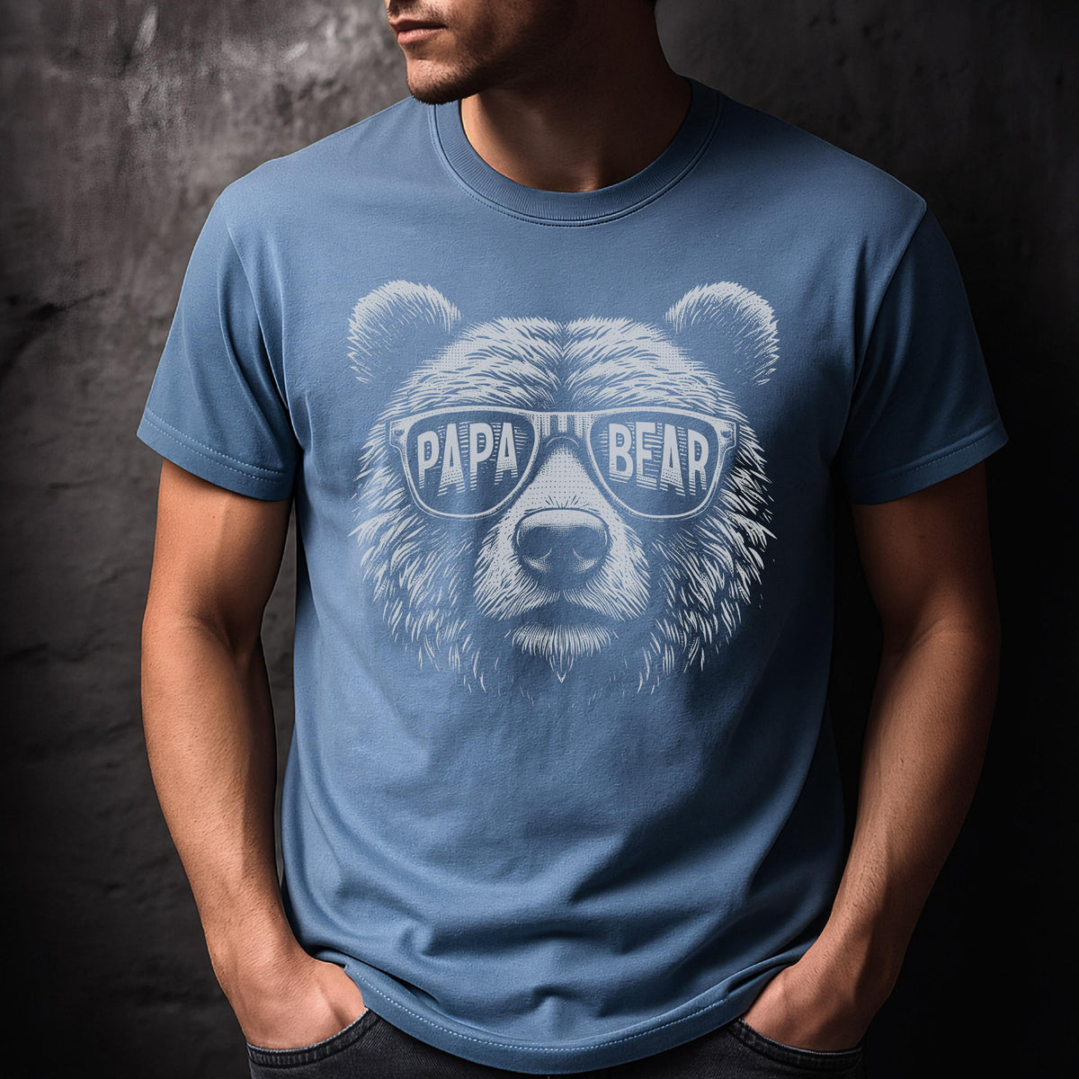 May include: A blue t-shirt featuring a bear face wearing sunglasses. The sunglasses have the words "PAPA BEAR" printed on them in white. The shirt is a solid color and has short sleeves.