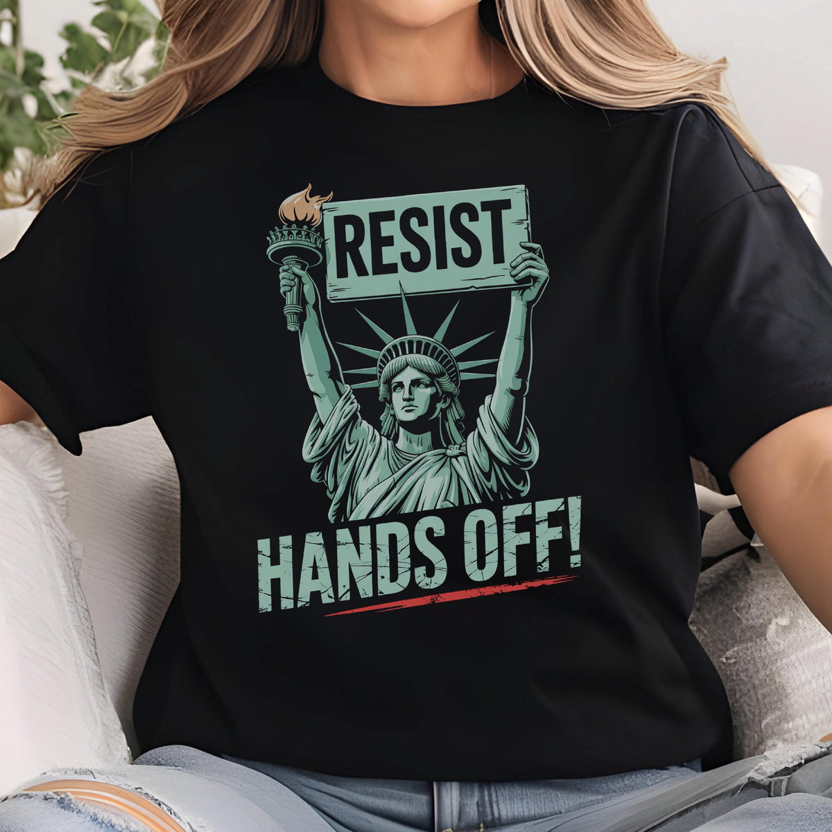 May include: Black t-shirt with a graphic of the Statue of Liberty holding a sign that says "Resist" and the text "Hands Off!" below.