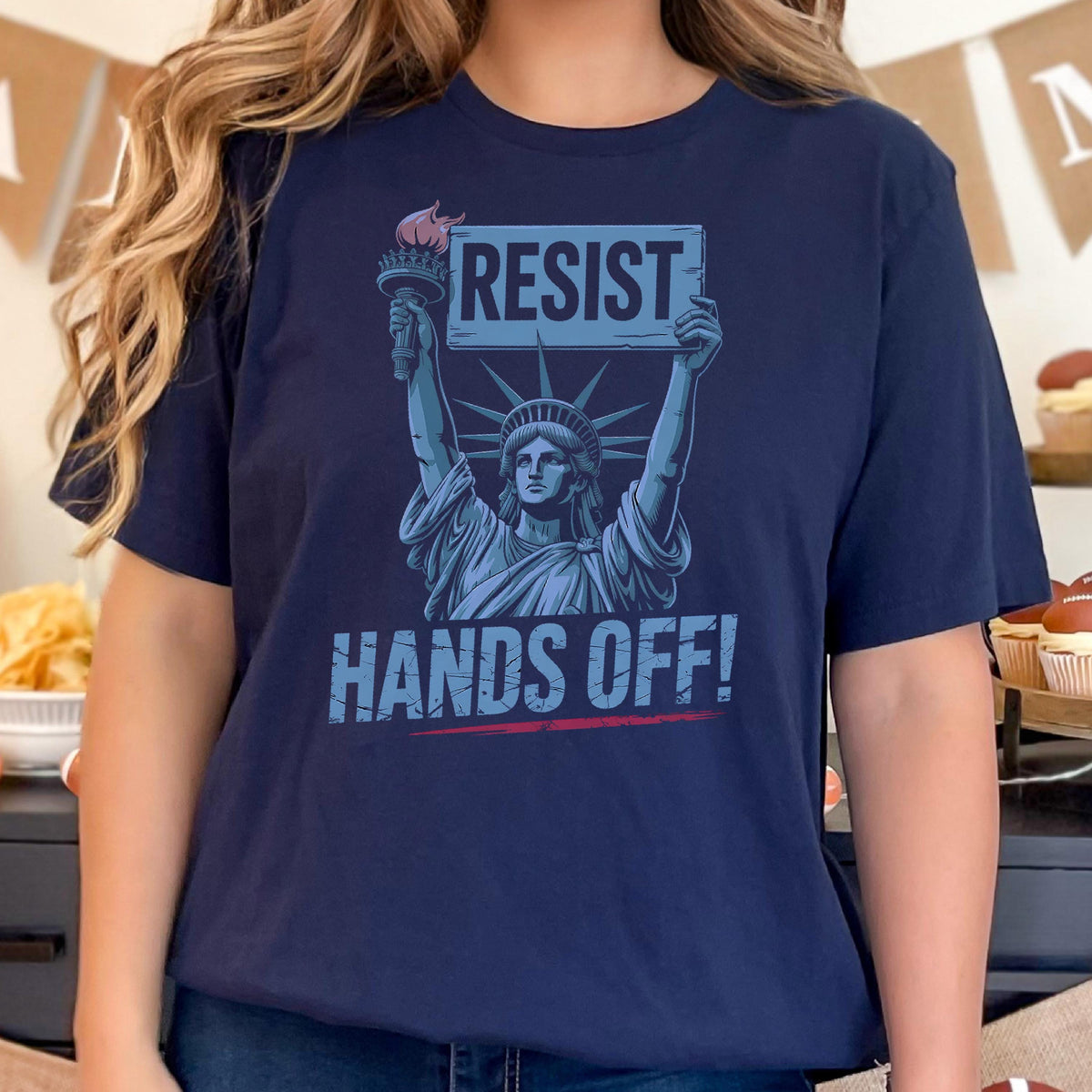May include: A navy blue t-shirt with a graphic of the Statue of Liberty holding a sign that says "Resist" and the text "Hands Off!" underneath.