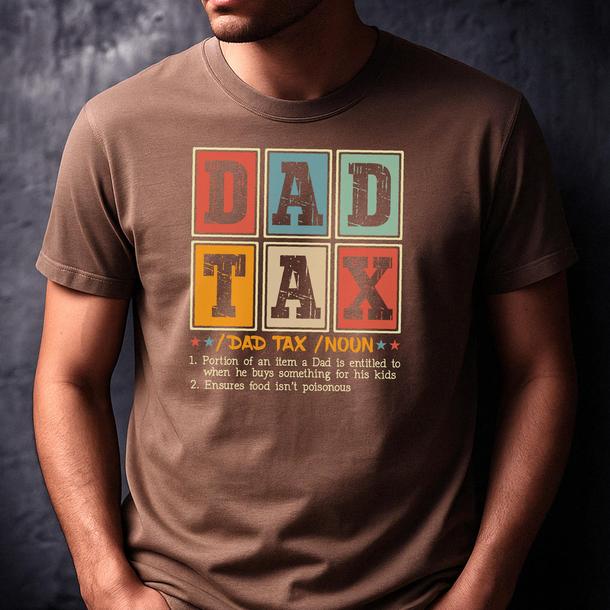 May include: Brown t-shirt with a colorful graphic that reads "DAD TAX" in a retro style. The graphic includes a definition of "DAD TAX" below the text. A fun and humorous gift for fathers.