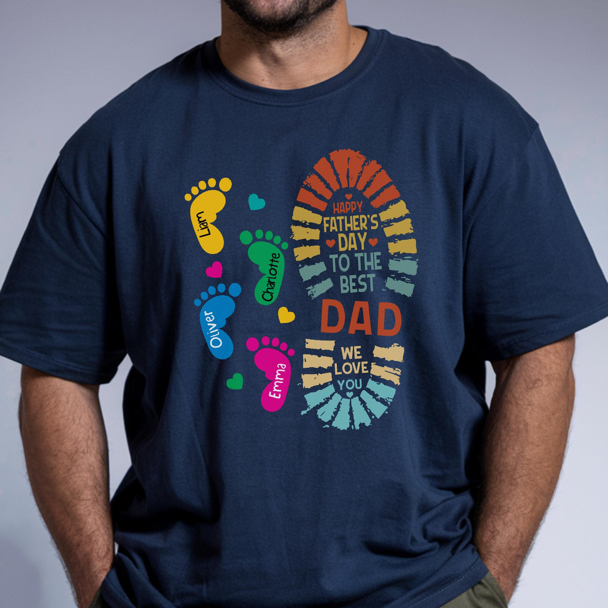 May include: Navy blue t-shirt with a colorful graphic for Father's Day. The design includes a large footprint with the text "Happy Father's Day to the Best Dad" and smaller footprints with names. Hearts are scattered around the footprints.