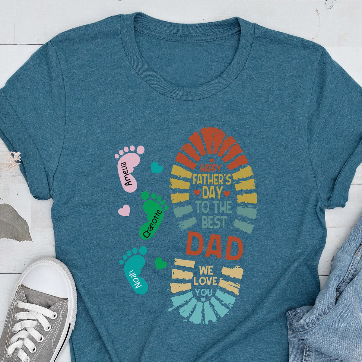 May include: Teal t-shirt with a colorful Father's Day design. The design includes a footprint shape with the text "Happy Father's Day to the Best Dad, We Love You." Footprints with names Amelia, Charlotte, and Noah are also featured.