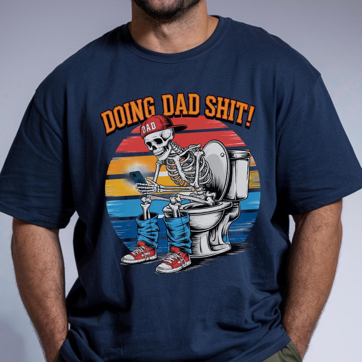May include: Navy blue t-shirt with a graphic of a skeleton wearing a red cap and blue jeans, sitting on a toilet while using a smartphone. The text "DOING DAD SHIT!" is above the skeleton.